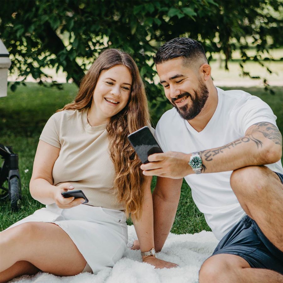 Par sitter i parken og ser på hverandres mobiltelefoner